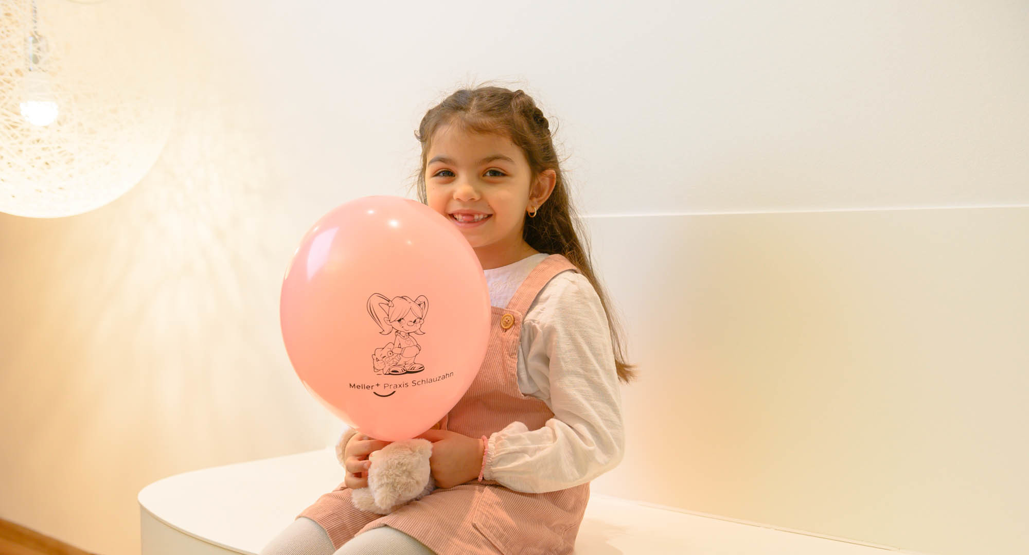 Kleines Mädchen mit Zahnlücke hält rosa Luftballon in Wartezimmer Meller_Schlauzahn_Impressionen_Z20_1298.jpg