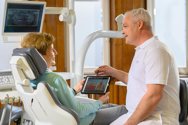 Zahnarzt Meller zeigt Seniorin auf Tablet den Ablauf der Parodontitisbehandlung