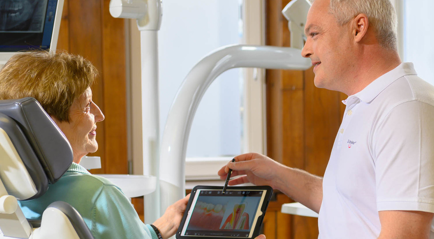 Zahnarzt Meller zeigt Seniorin auf Tablet den Ablauf der Parodontitisbehandlung