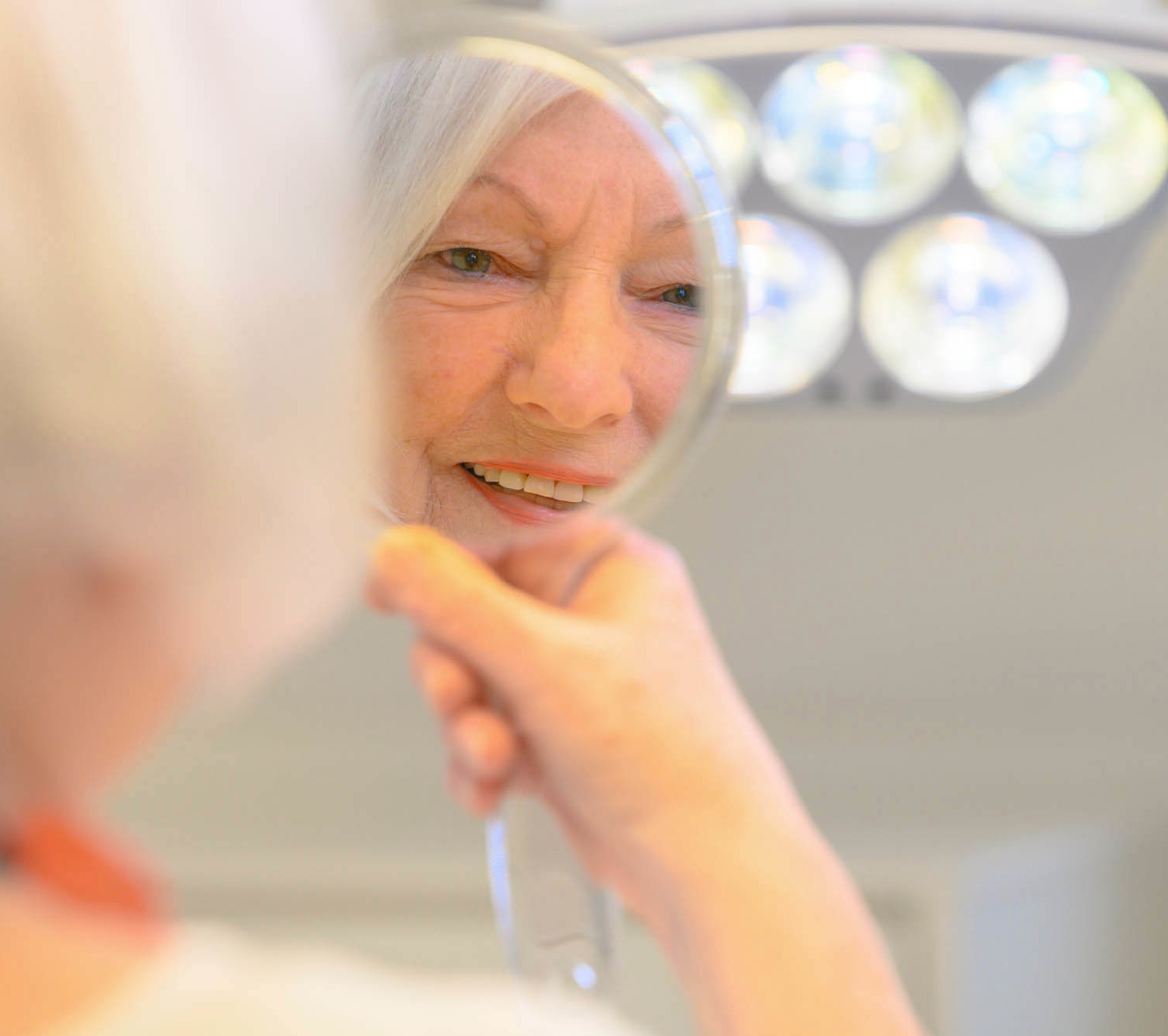 Seniorin schaut zufrieden in Handspiegel auf Zahnarztstuhl